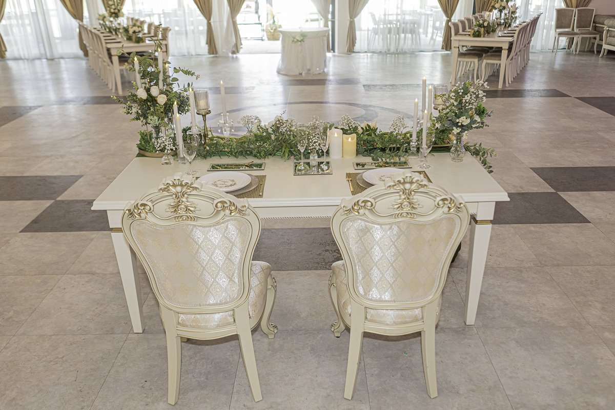 Gedeckter Brauttisch mit weißen Blüten, Kerzen und zwei Stühlen im Saal des Villa Restaurant Sömmerda