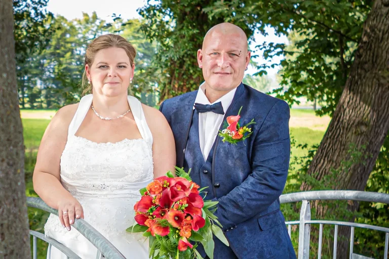 Brautpaar am Geländer mit leuchtend rotem Strauss, Hochzeitsfotografie Sömmerda
