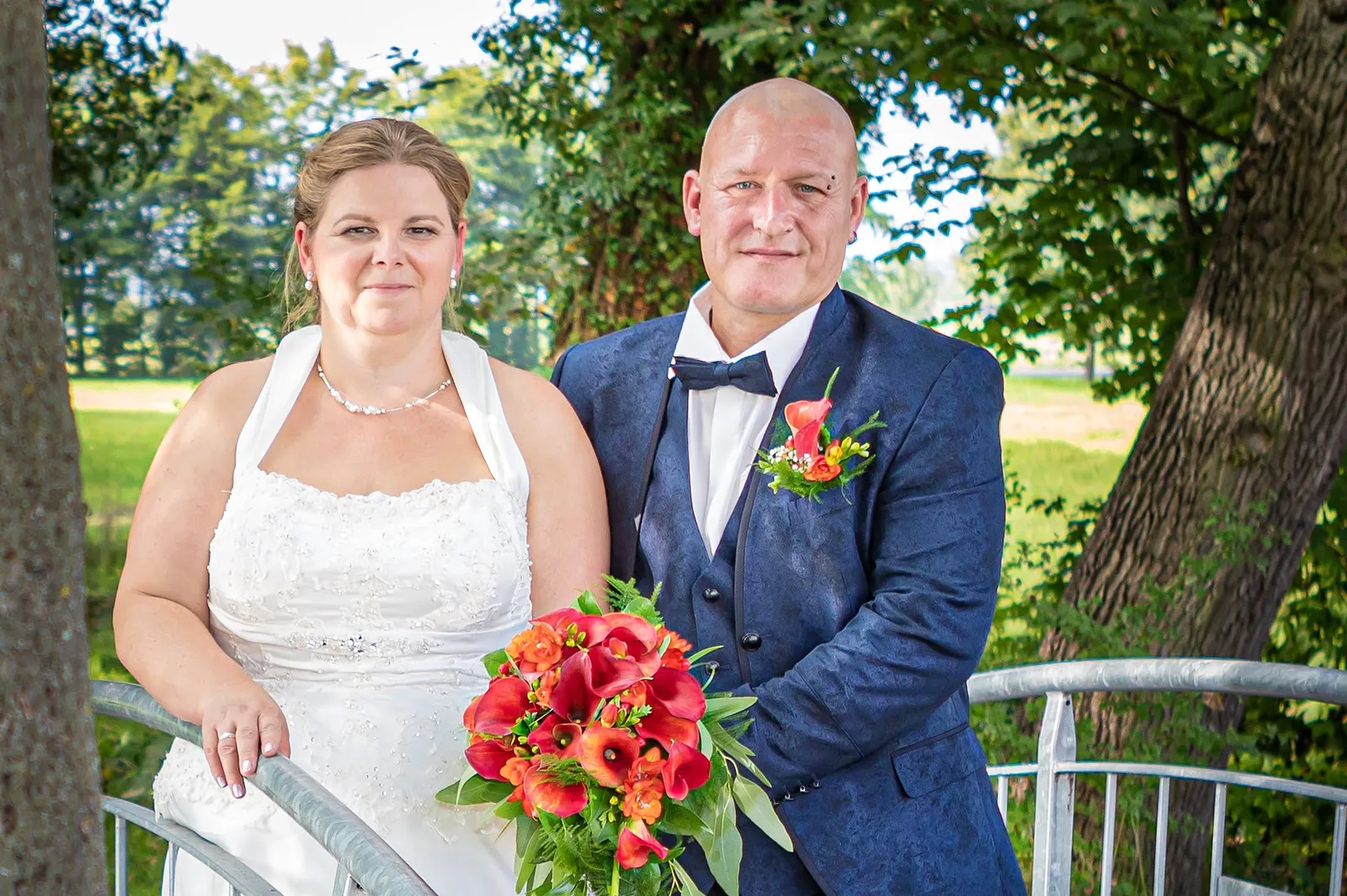 Brautpaar am Geländer mit leuchtend rotem Strauss, Hochzeitsfotografie Sömmerda