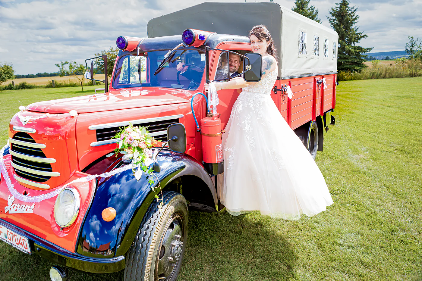 Braut vor dem roten Feuerwehr-Oldtimer auf der Wiese in Gebesee