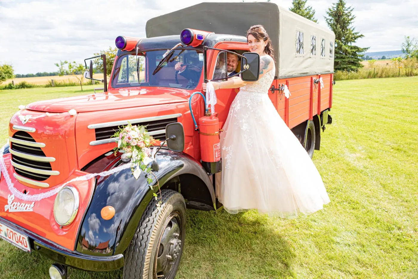 Braut vor dem roten Feuerwehr-Oldtimer auf der Wiese in Gebesee