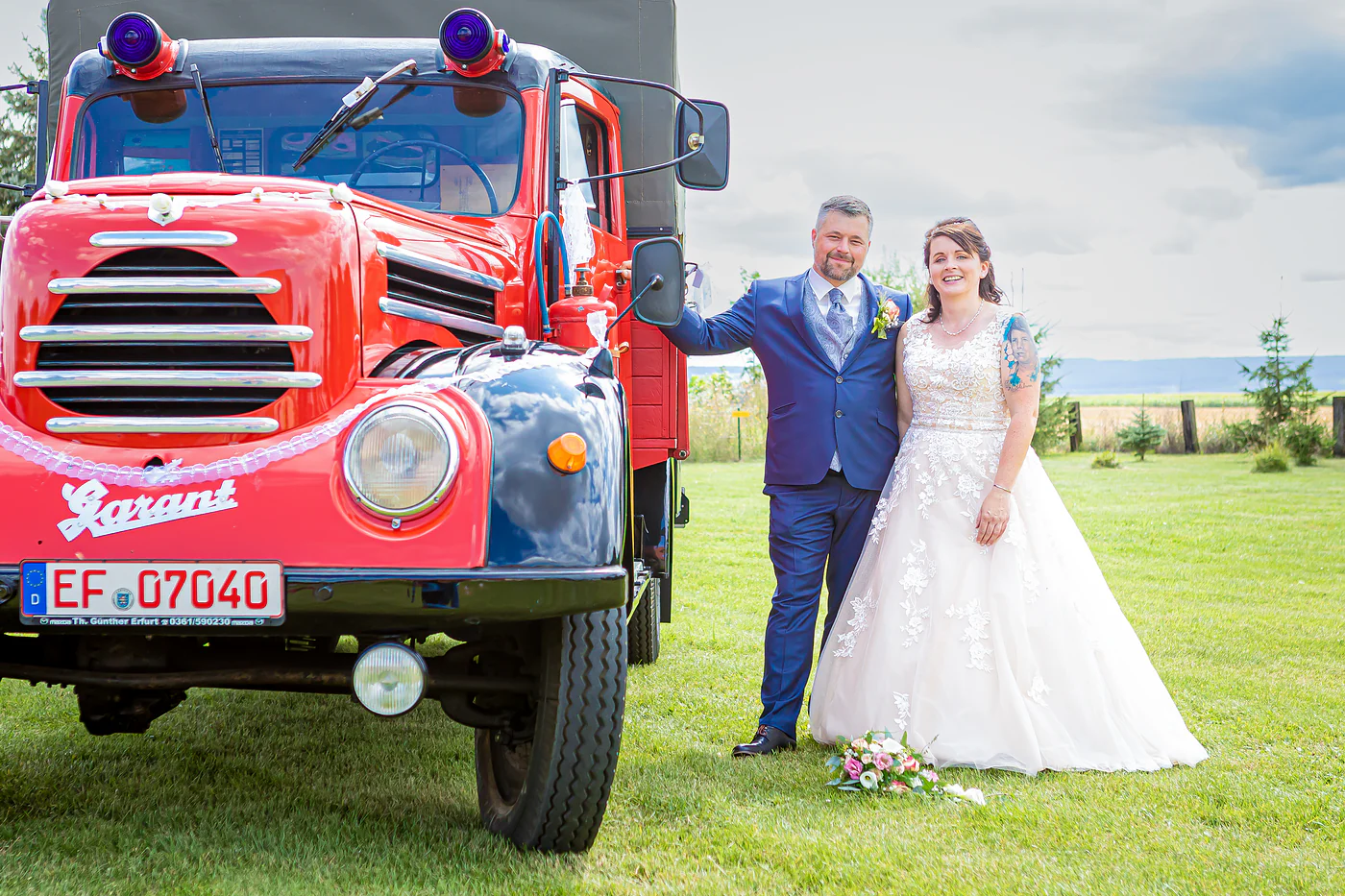 Brautpaar neben dem roten Robur Garant der Feuerwehr, der Br&auml;utigam mit der Hand am Au&szlig;enspiegel, Hochzeit in Gebesee