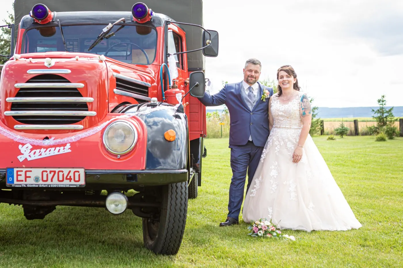 Brautpaar auf den Trittbrettern eines roten Robur Garant Feuerwehr-Oldtimers, Hochzeit in Gebesee