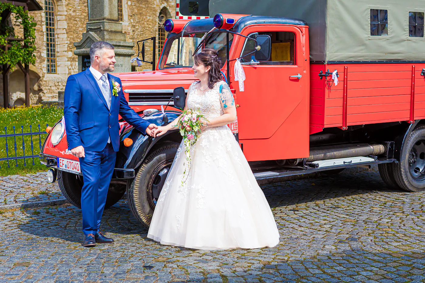 Brautpaar neben dem roten Feuerwehr-Oldtimer in der Nähe des Standesamts Gebesee
