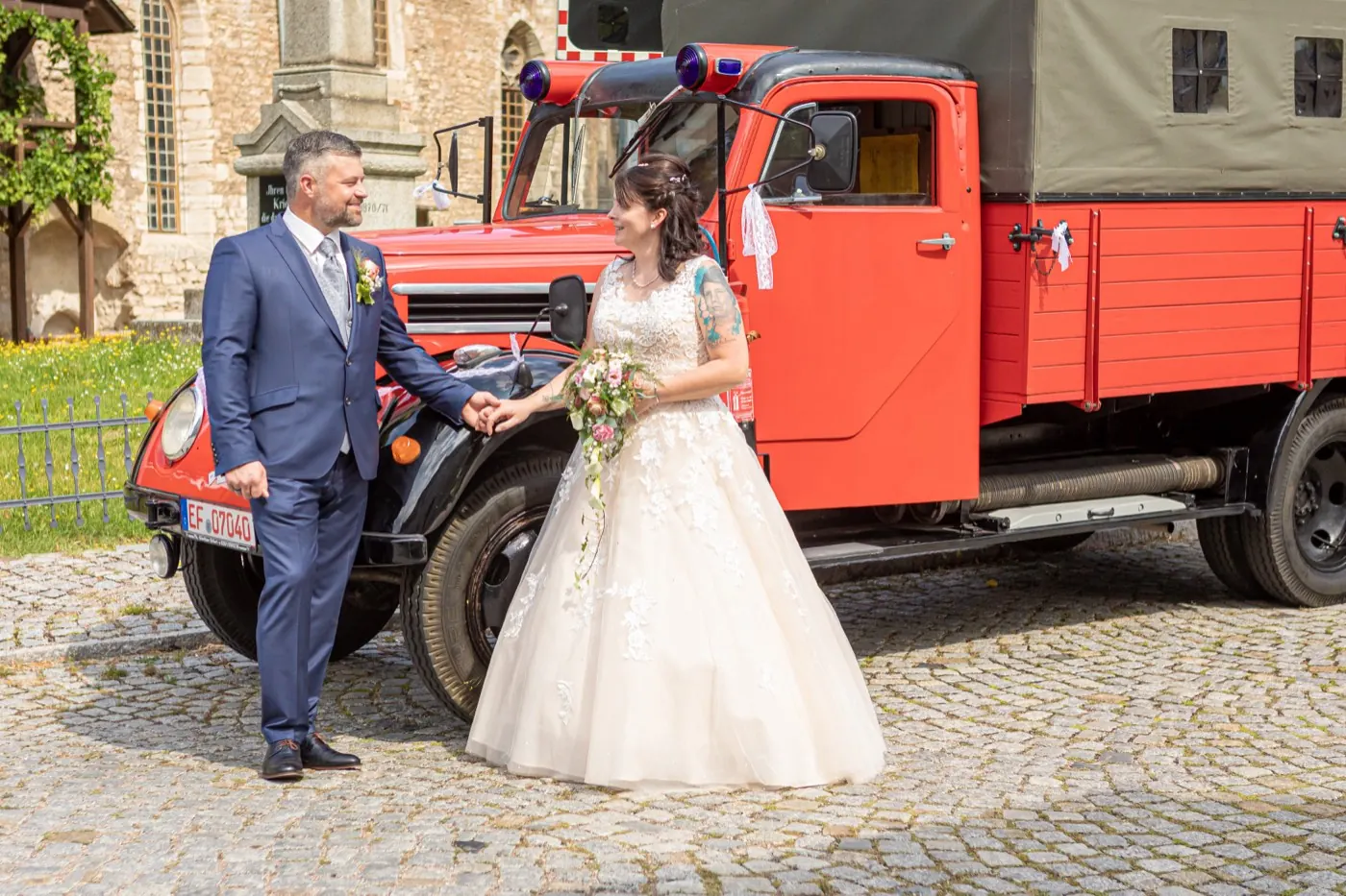 Brautpaar neben dem roten Feuerwehr-Oldtimer in der Nähe des Standesamts Gebesee