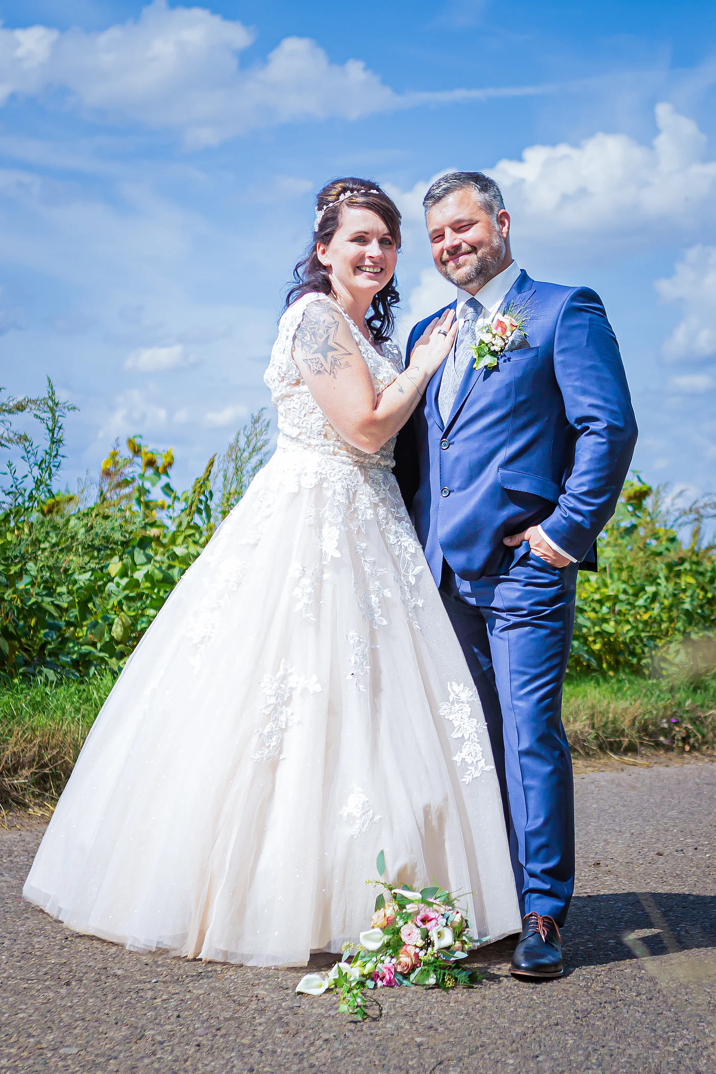 Brautpaar steht eng beieinander auf einem Feldweg, der Brautstrauß liegt vor ihnen am Boden, Hochzeit bei Gebesee
