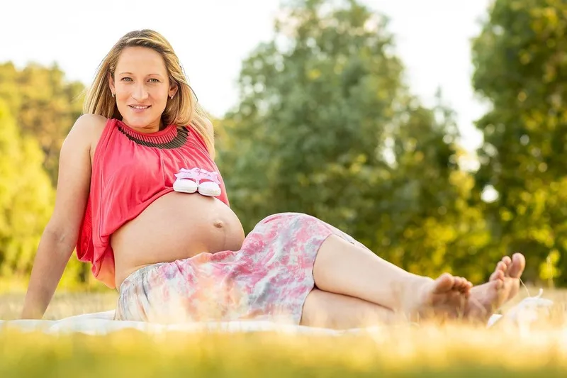 Schwangere Frau liegt entspannt auf einer Decke in der Sommerwiese, auf ihrem Babybauch stehen kleine rosa Babyschuhe, Babybauch Shooting Sömmerda Dirk Dittrich
