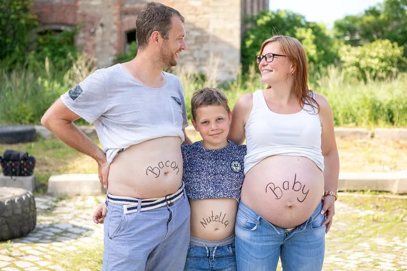 Vater, Sohn und schwangere Mutter zeigen lachend ihre Bäuche mit den Aufschriften Bacon, Nutella und Baby, Babybauch Shooting Sömmerda Dirk Dittrich