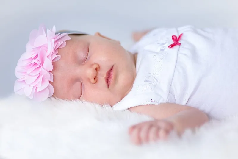 Schlafendes Neugeborenes mit rosa Blütenhaarband liegt friedlich auf einem weißen Fell, Babybauch Shooting Sömmerda Dirk Dittrich