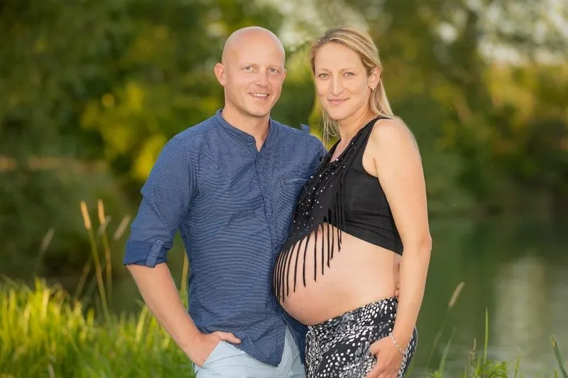 Lächelndes Paar am Seeufer im Grünen, die schwangere Frau trägt ein schwarzes Fransentop über dem freien Babybauch, Babybauch Shooting Sömmerda Dirk Dittrich
