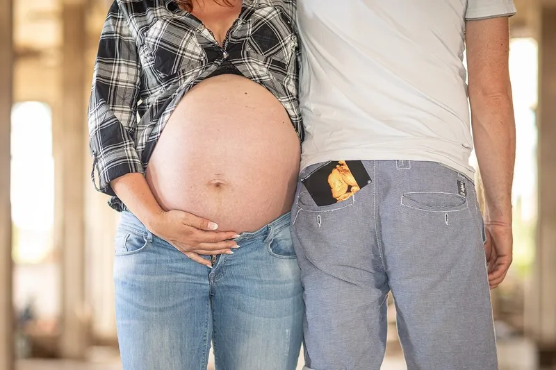 Werdende Eltern nebeneinander, sie hält ihren nackten Babybauch, in seiner Gesäßtasche steckt ein Ultraschallfoto, Babybauch Shooting Sömmerda Dirk Dittrich