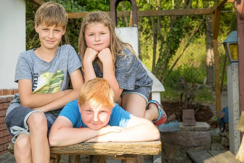 Drei Kinder posieren entspannt an einem rustikalen Holztisch im sommerlichen Garten, Familienfotograf Sömmerda Dirk Dittrich