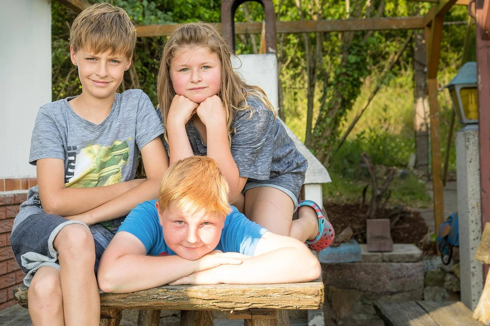 Drei Geschwister mit farblich abgestimmten Outfits in ruhigen Tönen beim Familienshooting im Garten in Thüringen