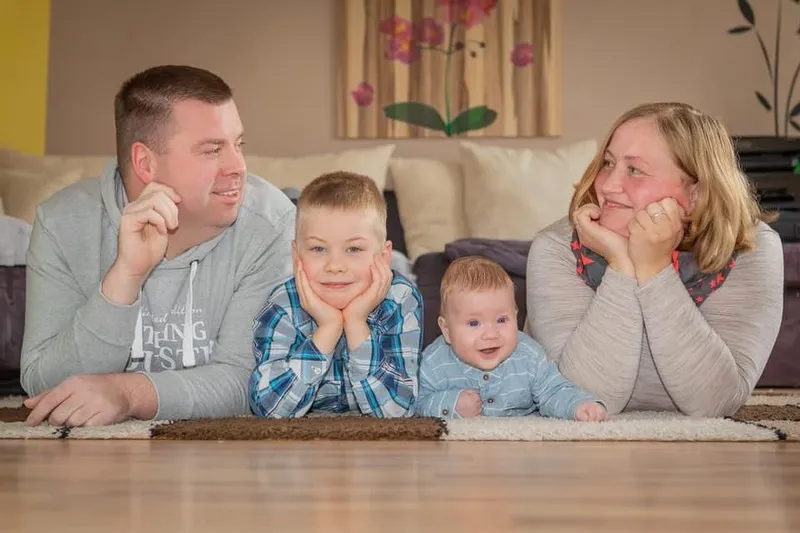 Eltern und zwei Söhne liegen bäuchlings auf dem Wohnzimmerteppich, die Eltern schauen liebevoll zu ihren Kindern, Familienfotograf Sömmerda Dirk Dittrich