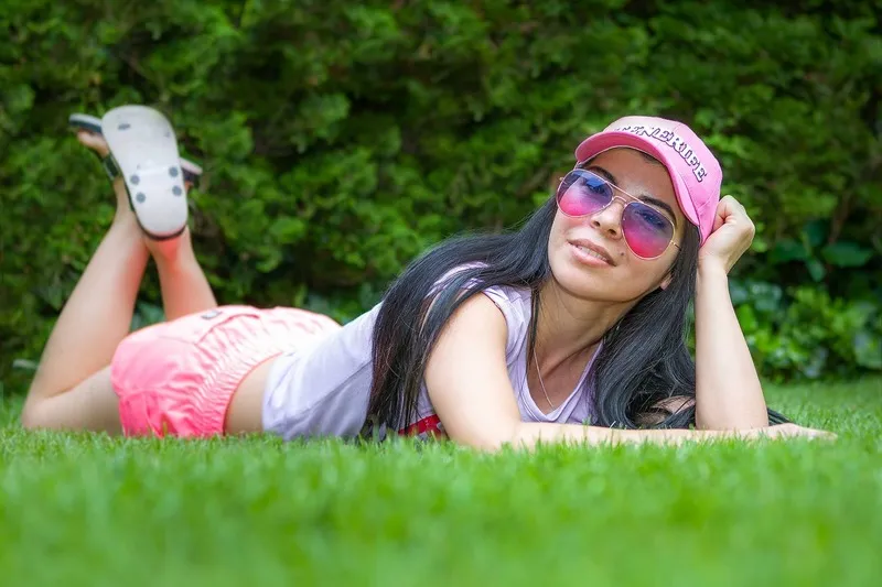 Junge Frau mit pinker Basecap und Sonnenbrille liegt entspannt auf einer grünen Wiese, Portraitfotograf Sömmerda Dirk Dittrich