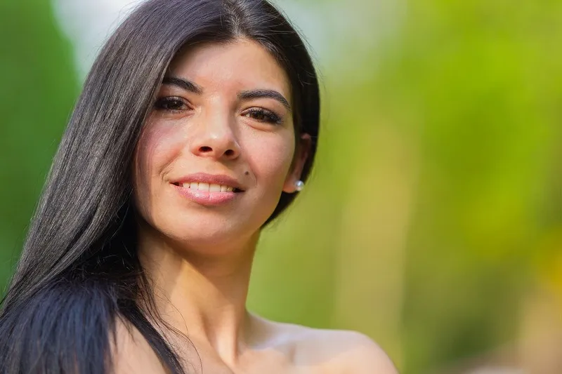 Nahaufnahme einer lächelnden Frau mit langen dunklen Haaren vor grünem Naturhintergrund, Portraitfotograf Sömmerda Dirk Dittrich