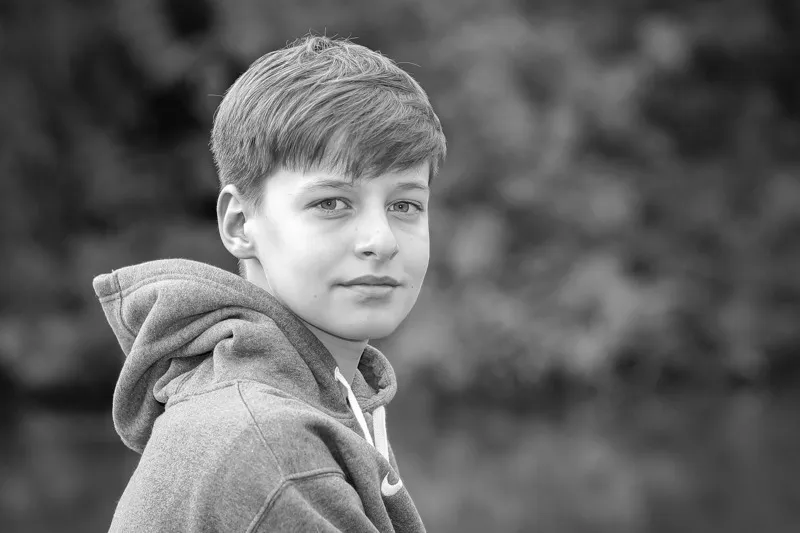 Schwarzweiß Portrait eines Jungen im Kapuzenpullover mit ruhigem Blick über die Schulter, Portraitfotograf Sömmerda Dirk Dittrich