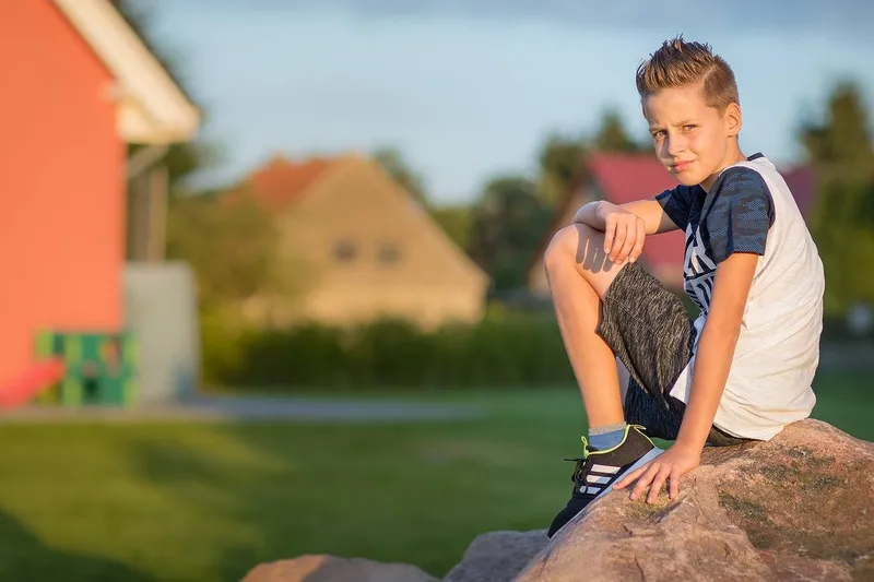 Junge sitzt im warmen Abendlicht auf einem großen Felsen, im Hintergrund Häuser und grüner Rasen, Portraitfotograf Sömmerda Dirk Dittrich