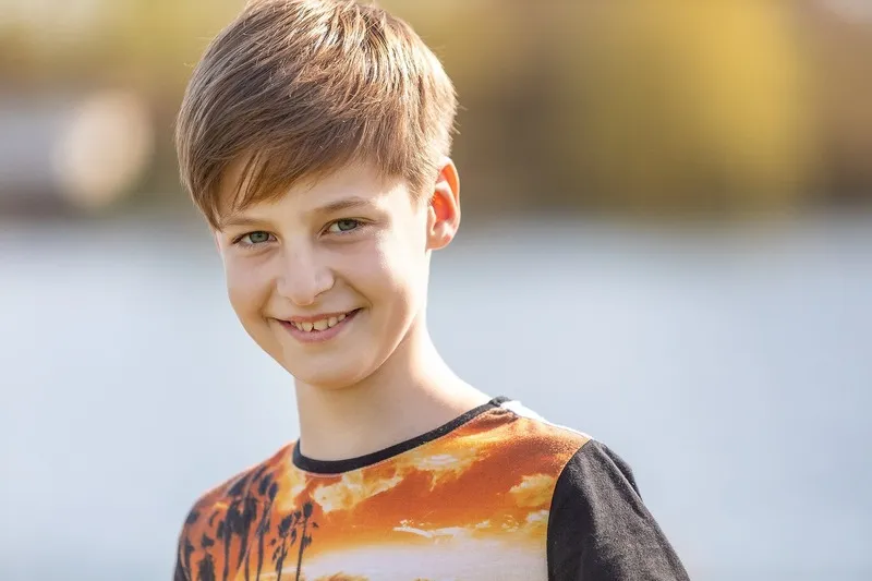 Lächelnder Junge im orangefarbenen Shirt vor hellem Wasser im Hintergrund, Portraitfotograf Sömmerda Dirk Dittrich