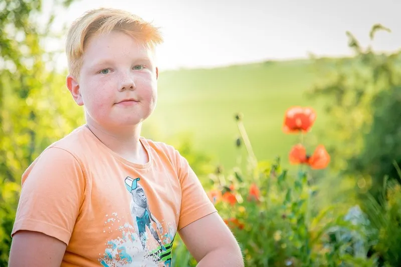 Rothaariger Junge mit Sommersprossen im orangefarbenen T-Shirt vor blühendem Mohn im Gegenlicht, Portraitfotograf Sömmerda Dirk Dittrich