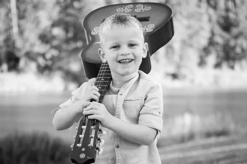 Schwarzweiß Portrait eines lachenden kleinen Jungen mit Gitarre über der Schulter, Portraitfotograf Sömmerda Dirk Dittrich