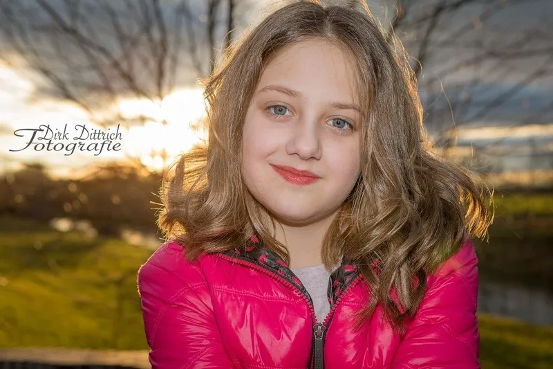 Mädchen in pinker Steppjacke lächelt sanft im warmen Gegenlicht der untergehenden Sonne, Portraitfotograf Sömmerda Dirk Dittrich