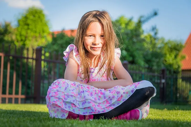 Kleines Mädchen im geblümten Sommerkleid sitzt lächelnd im Schneidersitz auf dem Rasen, Portraitfotograf Sömmerda Dirk Dittrich
