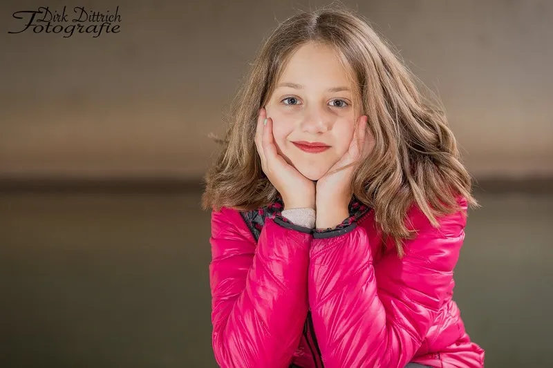 Mädchen in pinker Steppjacke stützt das Kinn in beide Hände und lächelt in die Kamera, Portraitfotograf Sömmerda Dirk Dittrich