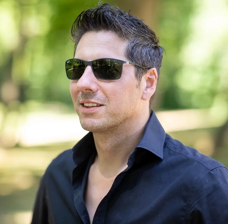 Lächelnder Mann mit Sonnenbrille im dunklen Hemd vor sommerlichem Park, Portraitfotograf Sömmerda Dirk Dittrich